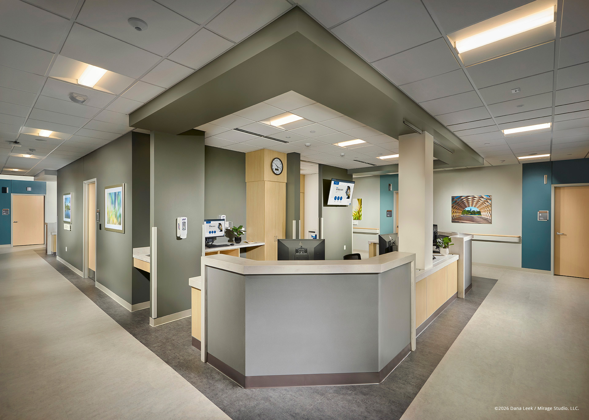 Centralized nurse station on an inpatient unit, with wraparound work surface, soft green and blue accent walls, and patient