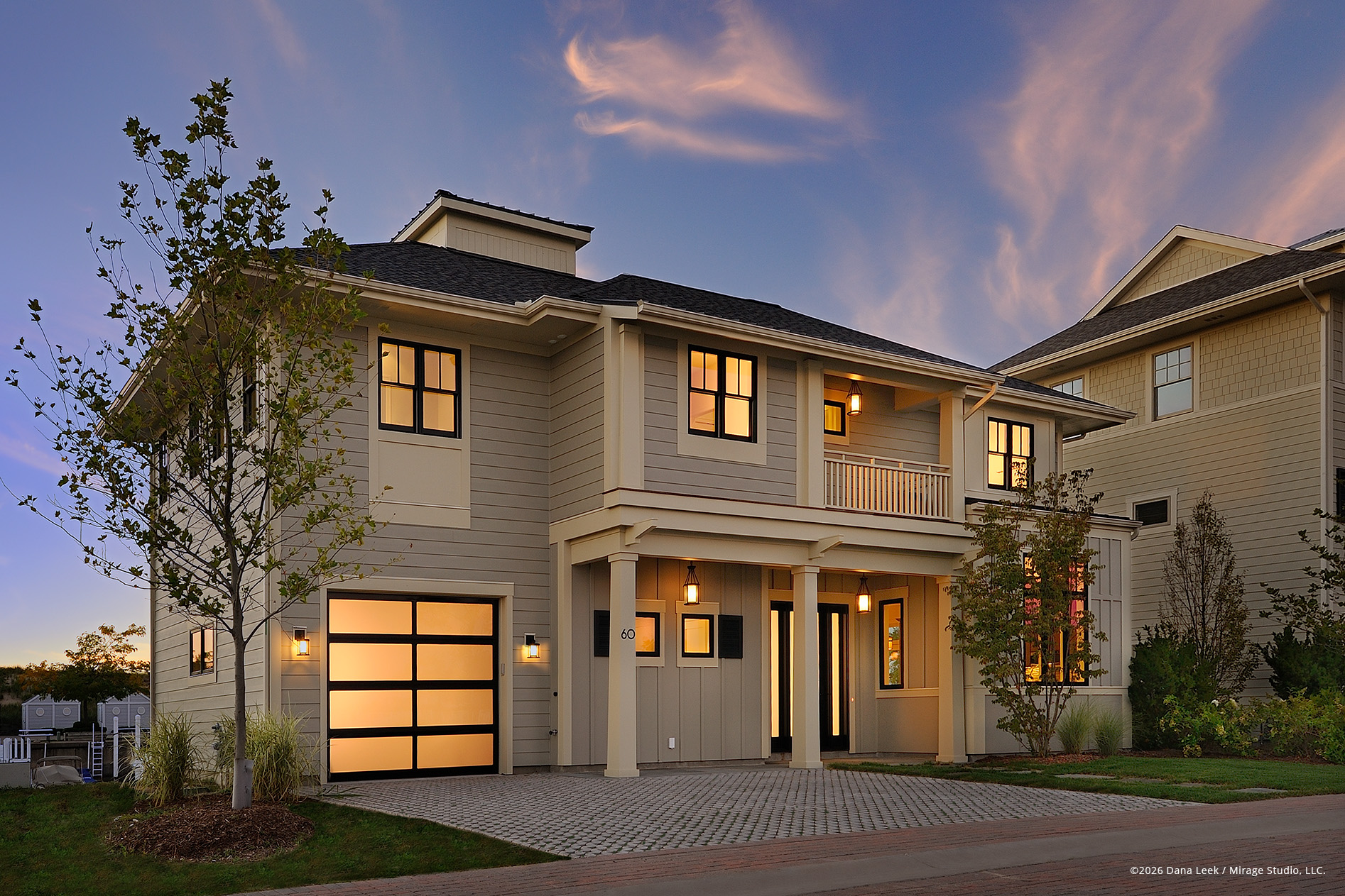 Twilight exterior of a contemporary coastal‑style residence, created from multiple exposures to balance the warm interior and exterior lighting with the pastel evening sky and softly lit siding.