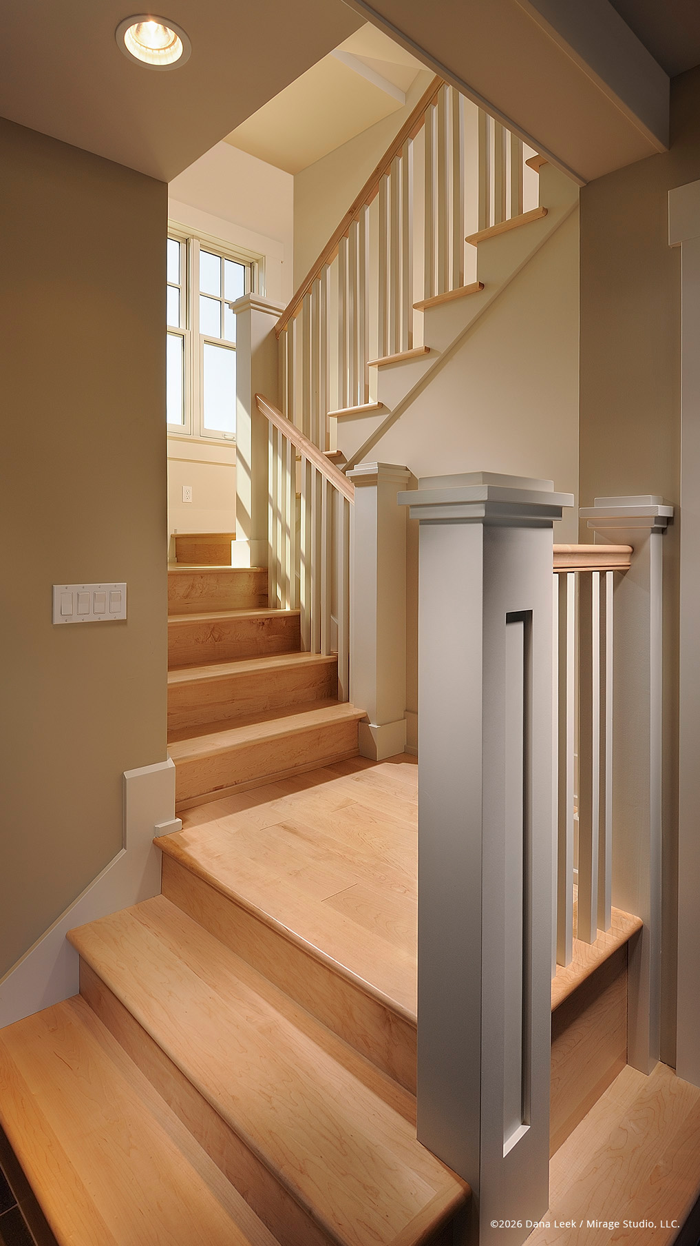 Warm residential stairway with maple treads, painted newel posts, and natural light spilling down from a landing window.