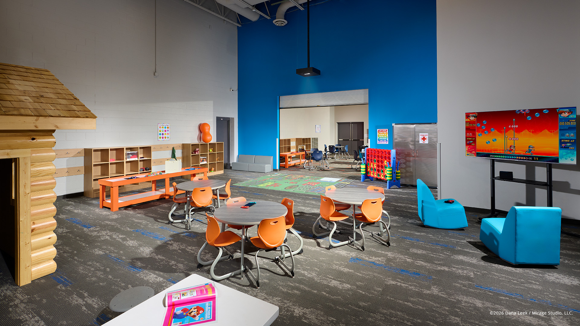 Colorful K–2 games room with flexible tables, reading nook, and gaming zone under a bright blue feature wall at the Boys & Girls Club.